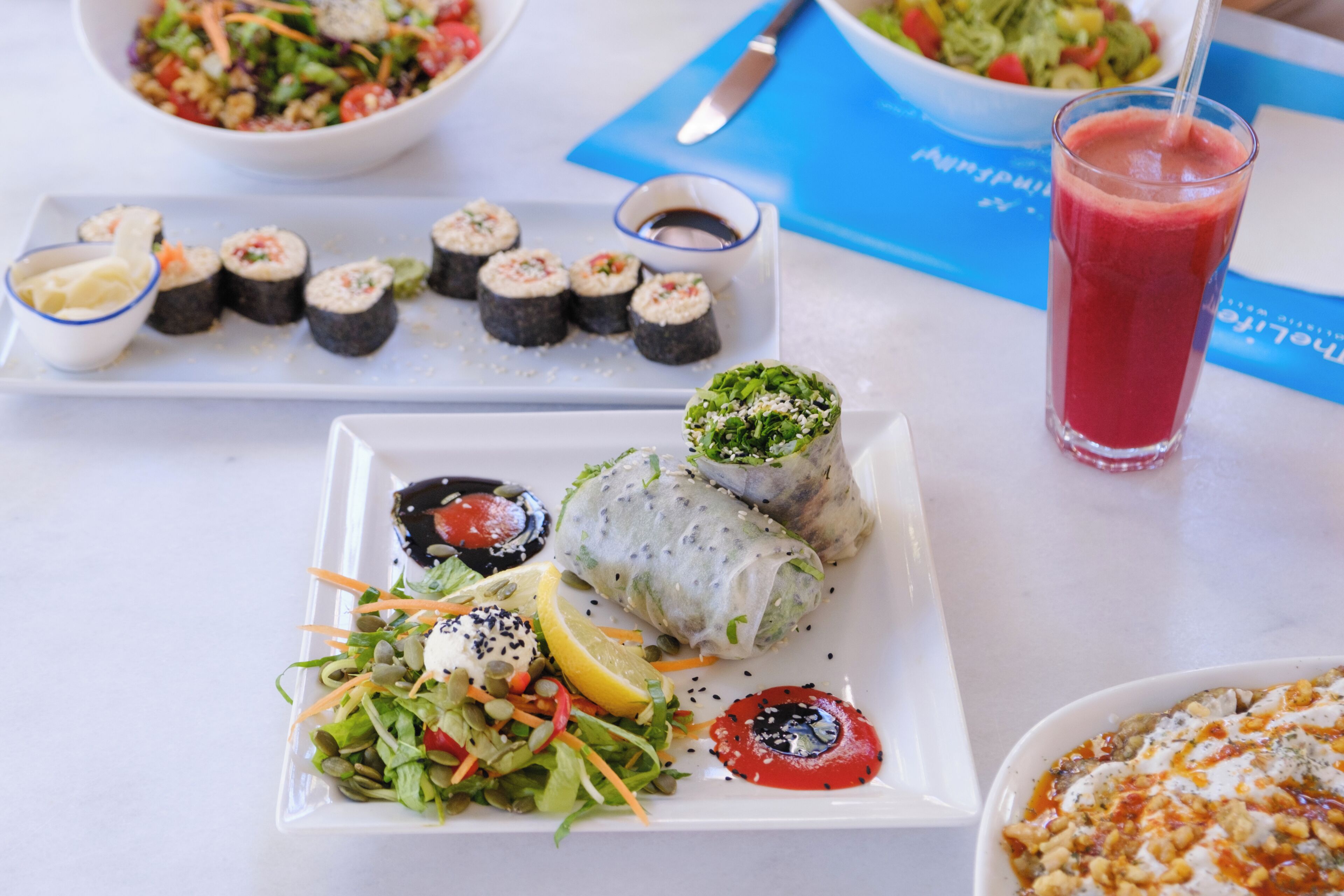 A table with various dishes including sushi, a salad, and a glass of red drink.