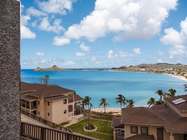 Vista costera con playa, cielo despejado y edificios con balcones que dan al mar.