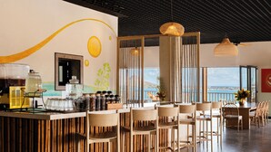 A modern bar area with a high ceiling, bamboo chairs, and a view of the sea.