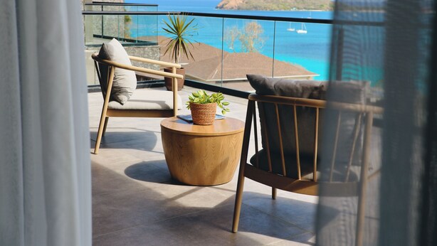 A balcony with a view of the ocean, a chair, a small table, and a potted plant.