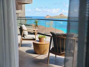 A balcony with a view of the ocean, a chair, a small table, and a potted plant.