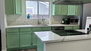 Una cocina con gabinetes verdes, una encimera blanca, una campana extractora de acero inoxidable y un ventanal con vistas al exterior.