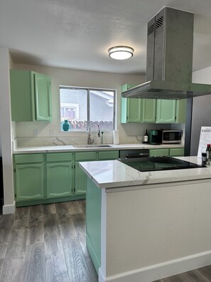A kitchen with green cabinets, a white countertop, a stainless steel range hood, and a window with a view of the outside.