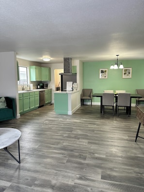 A modern kitchen with green cabinets, a central island, and a dining area with a table and chairs.