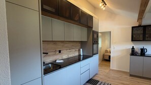 A modern kitchen with light grey cabinets, a black countertop, and a wooden backsplash. There is a black and white patterned rug on the floor. - Your time-out with a view of the Alps and the Kander (Kandergrund)