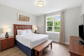 Ein Hotelzimmer mit Bett, Nachttischen, einer Bank, einem Fernseher und einem Fenster mit Vorhängen.
