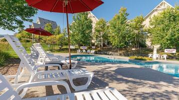 A pool area with lounge chairs and umbrellas, surrounded by trees and buildings.