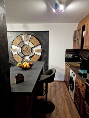 Une cuisine moderne avec un îlot central, des meubles en bois, un lave-linge et une grande horloge murale.