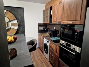 Une cuisine compacte équipée d’un lave-linge, d’un four à micro-ondes et de meubles de rangement en bois.