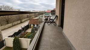 Een balkon met een tafel en stoelen, uitzicht op een weg en een kleine tuin.