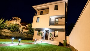 Een modern gebouw met twee verdiepingen, een plat dak, een balkon op de bovenverdieping en een helder verlichte ingang.