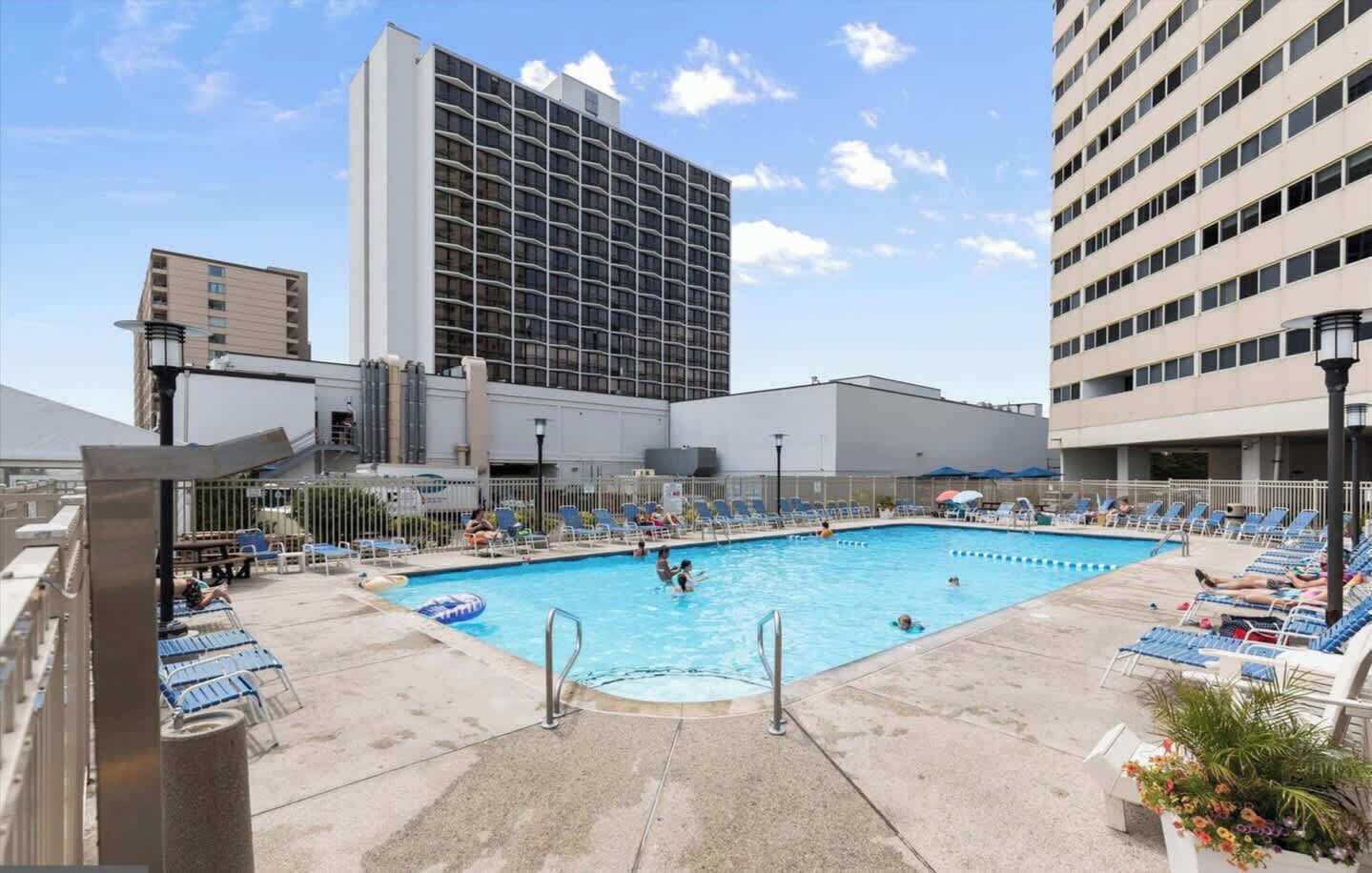 A hotel pool area with a large pool, lounge chairs, and a tall building in the background.