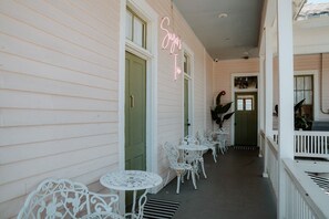 A covered porch with white metal chairs and tables, a neon sign, and a green door. - Sugar`s Inn Room #4 | Romantic Stay Near Galveston Cruise Port & Downtown (Galveston)