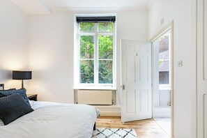 Ein Schlafzimmer mit einem Bett, einem Fenster, einem Heizkörper und einer Tür zu einem anderen Raum.