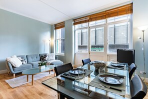 Ein modernes Wohnzimmer mit Glastisch, Sofa und großen Fenstern mit Jalousien.