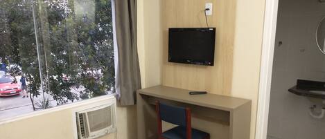 Une chambre d’hôtel comprenant un lit, un bureau avec une chaise, une télévision et une fenêtre donnant sur la rue.
