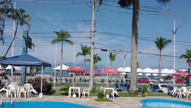 Une piscine entourée de palmiers et d’une clôture, avec des chaises longues et des parasols.