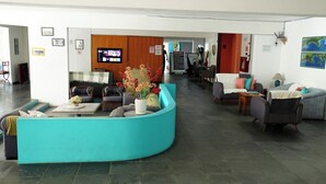 Un hall d  ’hôtel doté d’un comptoir d’accueil turquoise aux lignes courbes, de plusieurs espaces de détente, d’un téléviseur et d’un écran numérique.