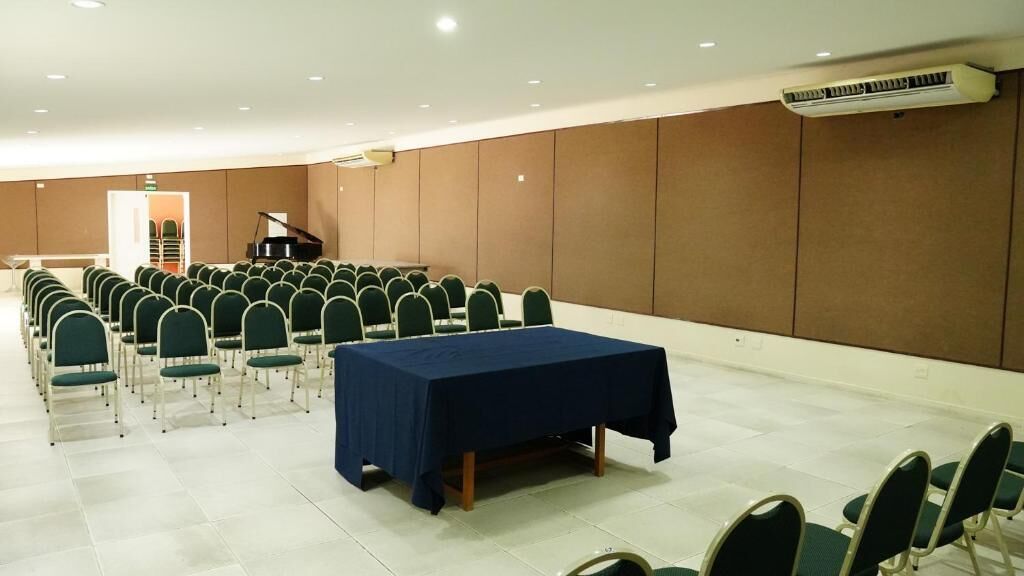 A conference room with rows of chairs, a table, and a piano.