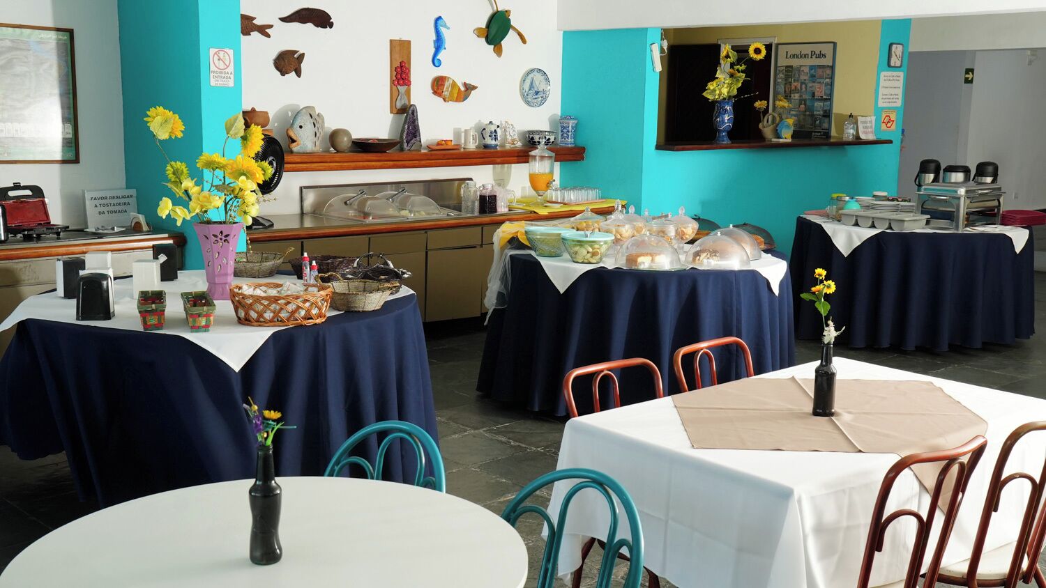A restaurant with multiple tables, some covered with blue tablecloths, and a kitchen area in the background.