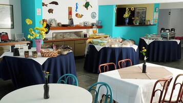 A restaurant with multiple tables, some covered with blue tablecloths, and a kitchen area in the background.