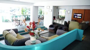 Un hall d’hôtel moderne doté d’un espace salon aux lignes courbes, d’un téléviseur à écran plat et d’une vue sur l’espace salon extérieur.