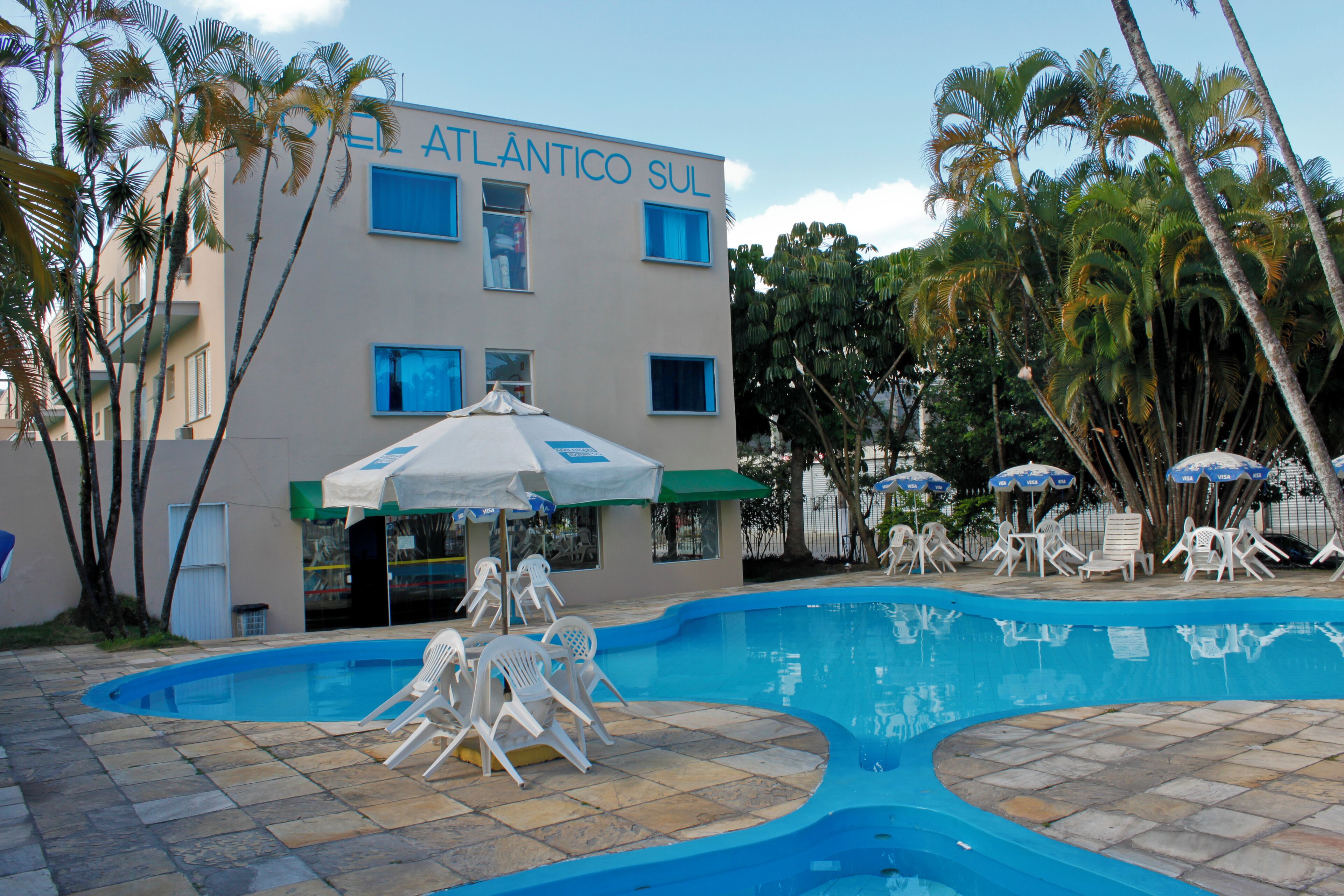 A hotel with a swimming pool, outdoor seating, and palm trees.