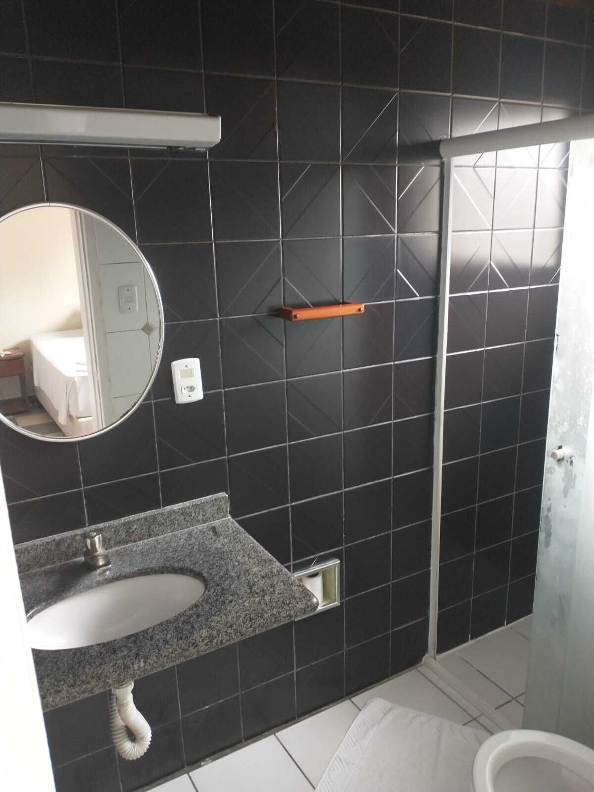 A bathroom with a dark tiled wall, a white sink with a granite countertop, a mirror, a towel rack, and a shower area.