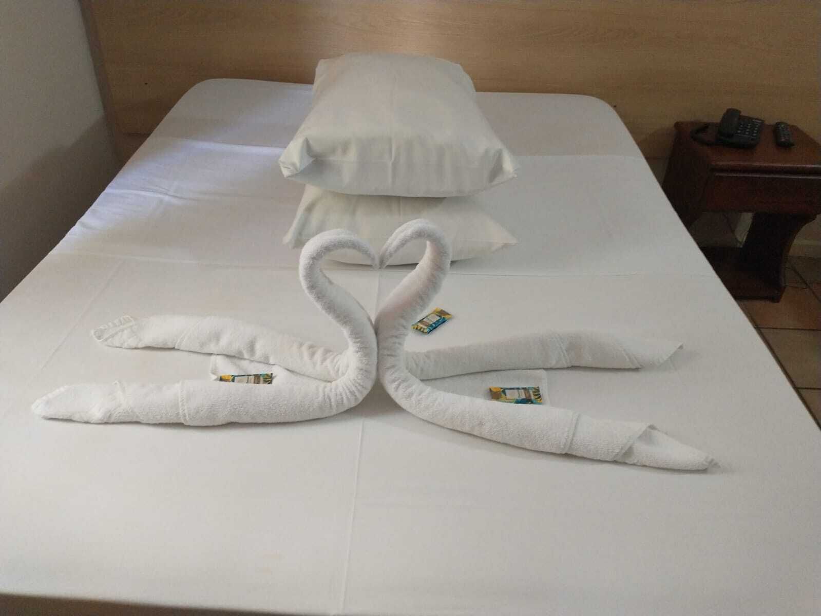 A hotel room with a neatly made bed, pillows, and a small bedside table with a telephone and remote controls.