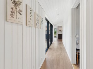Ein Korridor mit weißem Holzvertäfelung, Holzdielenboden und gerahmten Pflanzenabbildungen an der Wand.