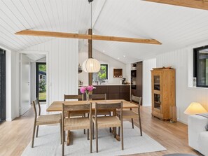 Eine moderne Küche mit Holzbalken, einem Essbereich mit Tisch und Stühlen und Blick durch eine offene Tür.