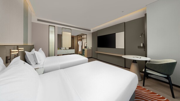 Une chambre d’hôtel avec deux lits, un bureau, une chaise, une télévision et un grand miroir.