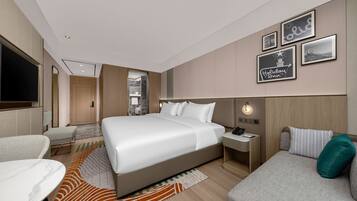 Habitación de hotel con una cama grande, un escritorio, una silla, un sofá y un televisor.