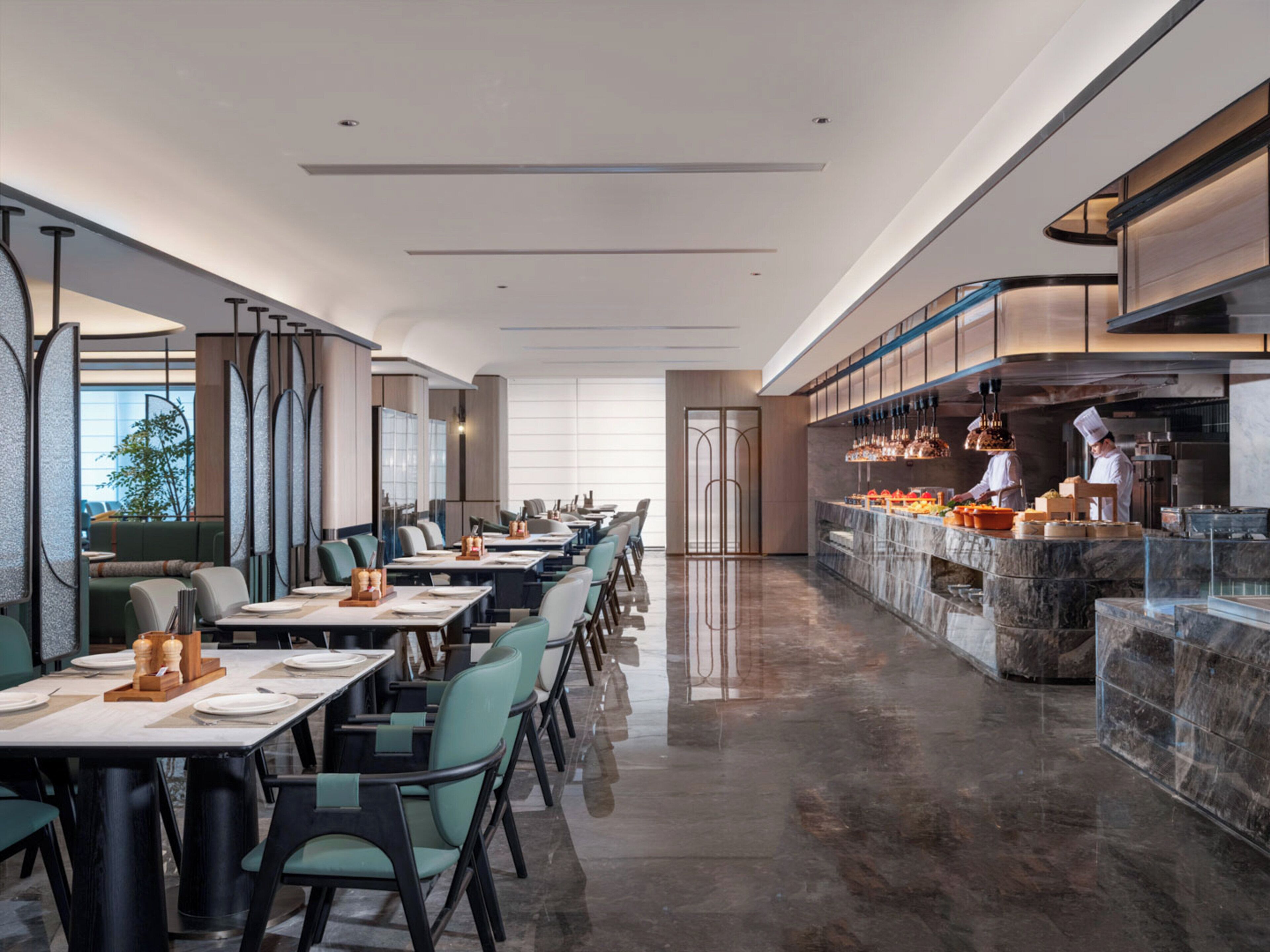 A modern restaurant with a long counter, multiple tables, and a kitchen area.
