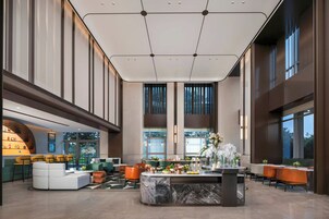 Un lobby espacioso con un mostrador de recepción de mármol central, zonas de estar y grandes ventanales con vistas.