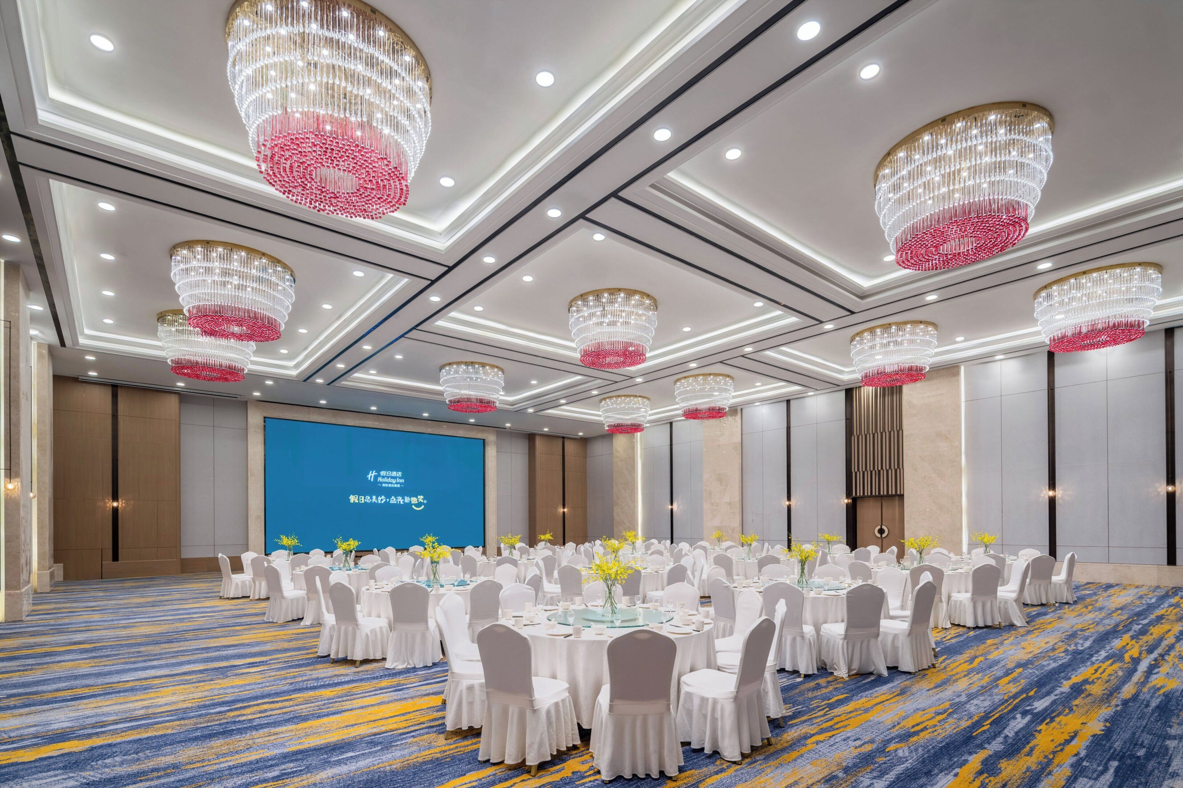 A conference room with round tables, white chairs, and chandeliers.