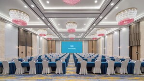 Une salle de conférence avec des rangées de tables, des chaises et un grand écran à l’avant.