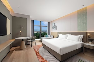 A modern hotel room with a large bed, a desk, a chair, and a view of the city.