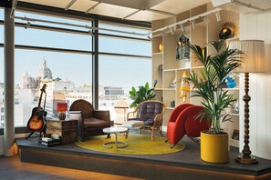 Ein modernes Wohnzimmer mit Blick auf die Stadt, ausgestattet mit einer Couch, Sesseln, einem Couchtisch und einem Bücherregal.