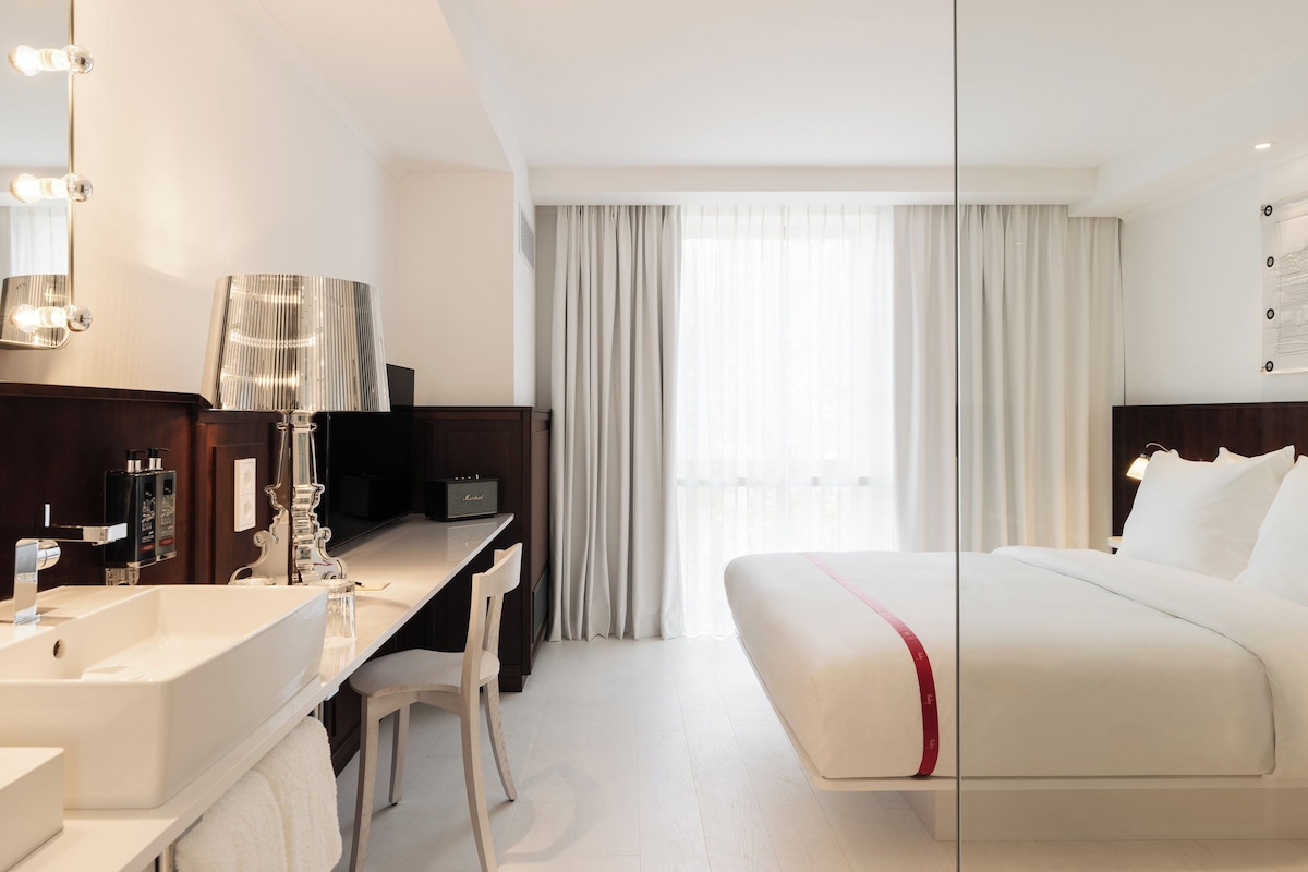 Ein Hotelzimmer mit Bett, Schreibtisch, Stuhl, Schminktisch und Spiegel sowie einem Fenster mit Vorhängen.
