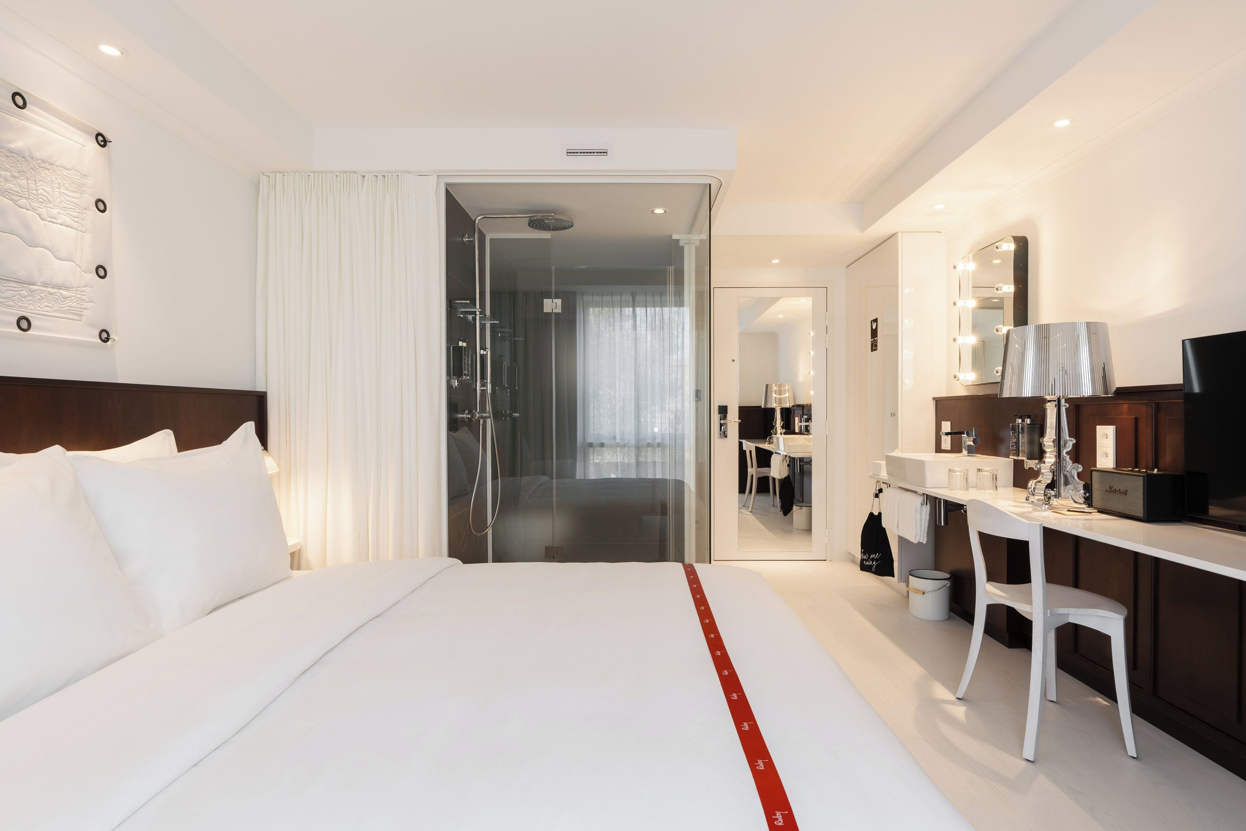 Habitación de hotel moderna con una cama grande, un escritorio con espejo e iluminación, y zona de ducha.