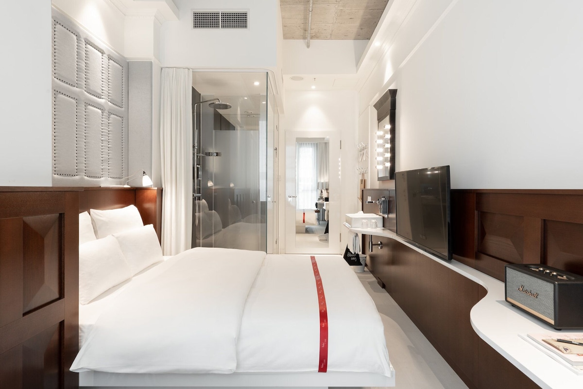 Une chambre d’hôtel comprenant un lit, une coiffeuse avec un miroir, une télévision et un espace douche.