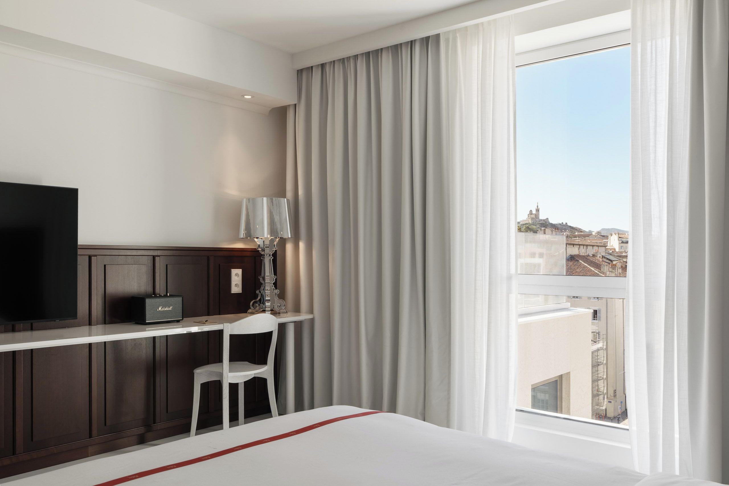 Una habitación de hotel con una cama, un escritorio con una silla, un televisor y una ventana con cortinas.