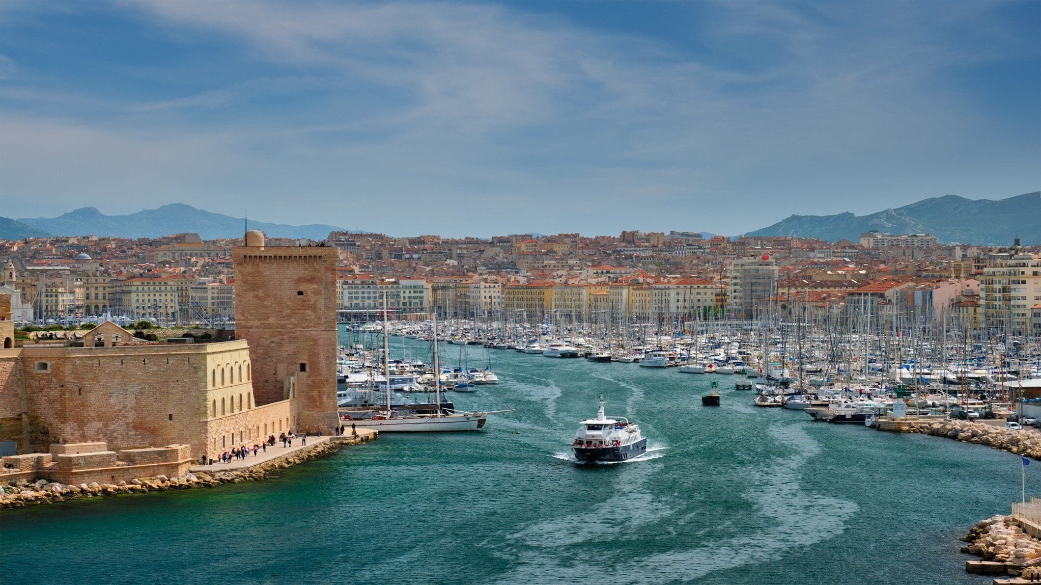 A harbor with boats, a castle-like structure, and a cityscape in the background.