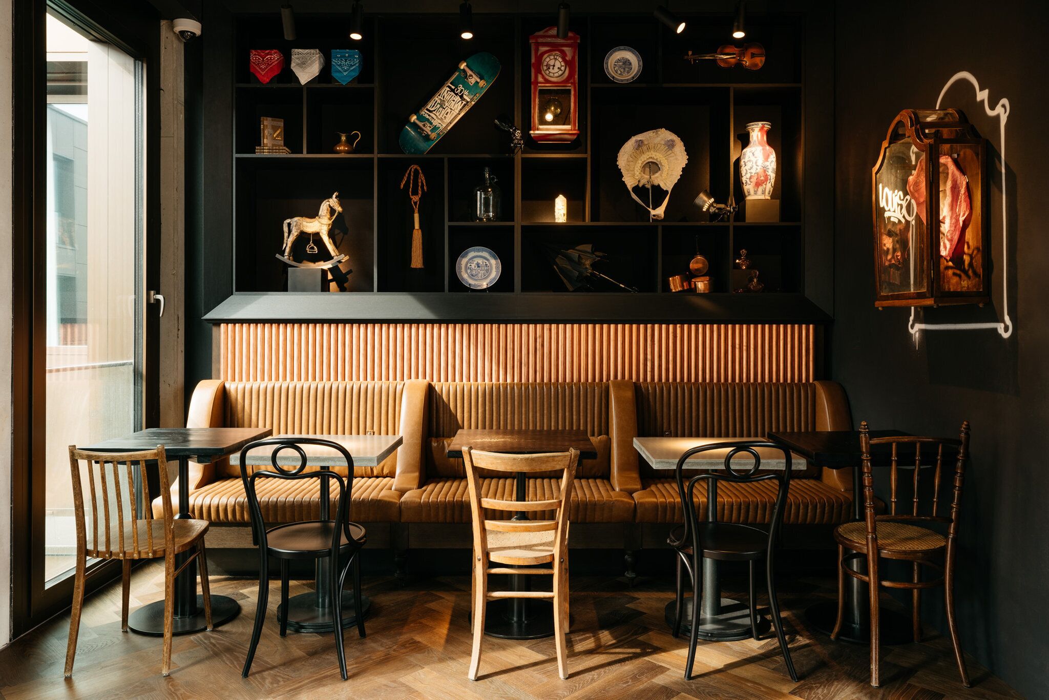A cozy seating area with a sofa and chairs, a wooden floor, and a wall with shelves displaying various items.