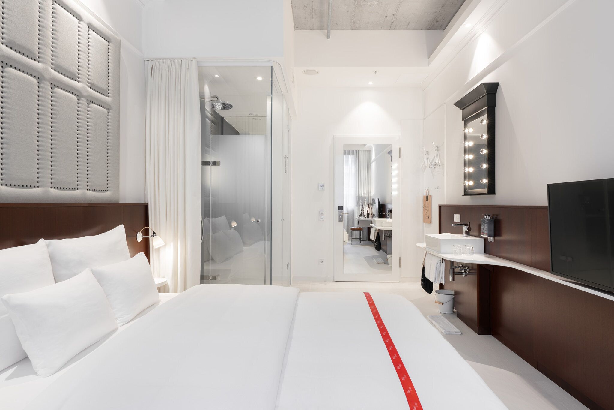 A modern hotel room with a large bed, a bathroom with a vanity, and a walk-in closet.