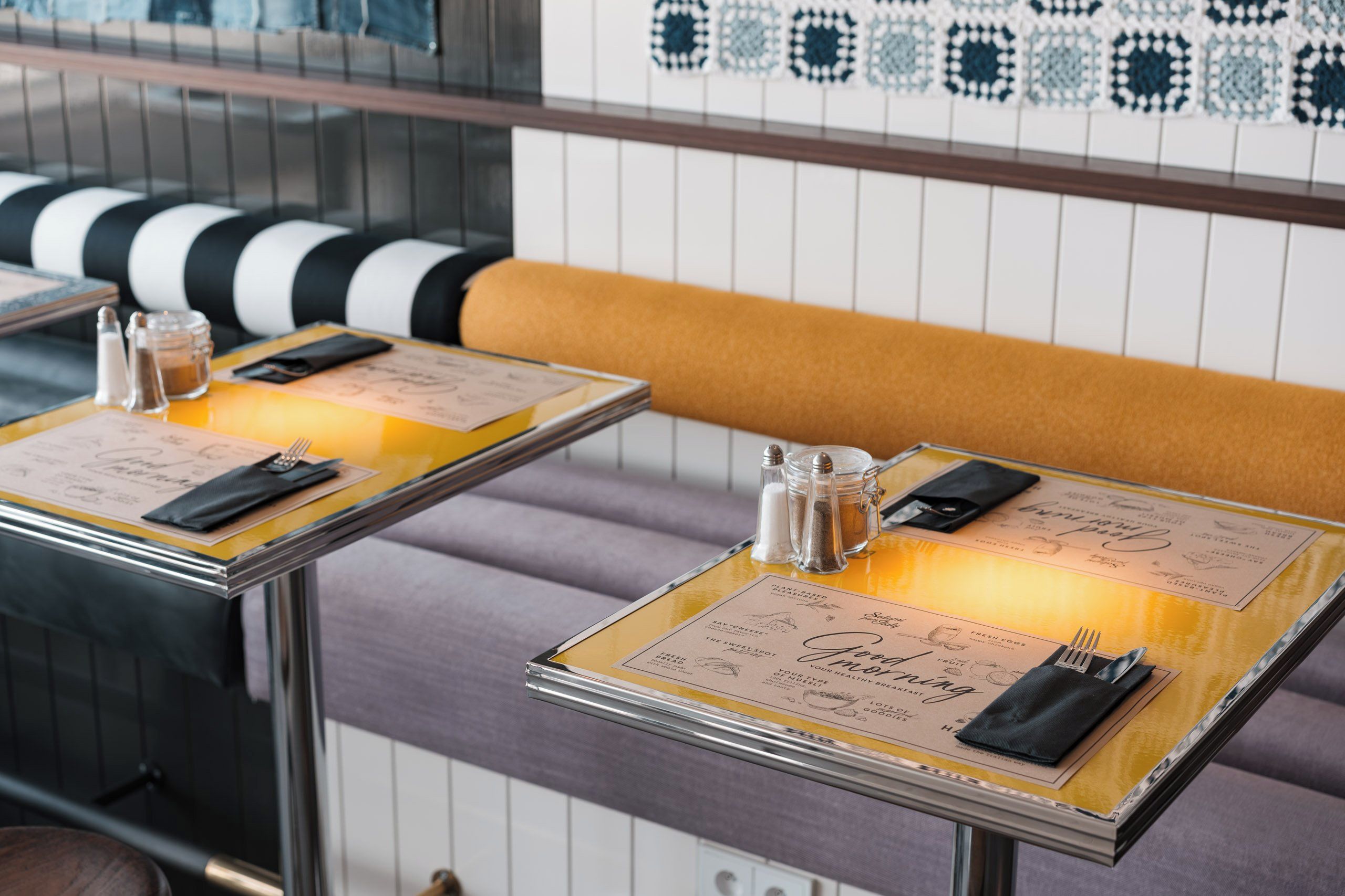 L’intérieur d’un restaurant, avec deux tables dressées pour le service, chacune agrémentée d’un menu, de salières et de poivrières, ainsi que de couverts.