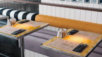 A restaurant interior with two tables set for dining, each with a menu, salt and pepper shakers, and cutlery.