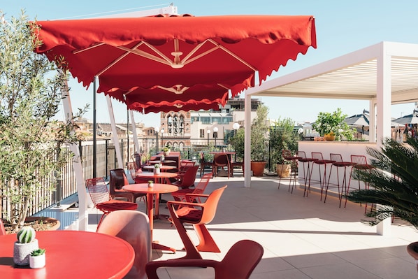 An outdoor seating area with red chairs and tables, a red umbrella, and potted plants.
