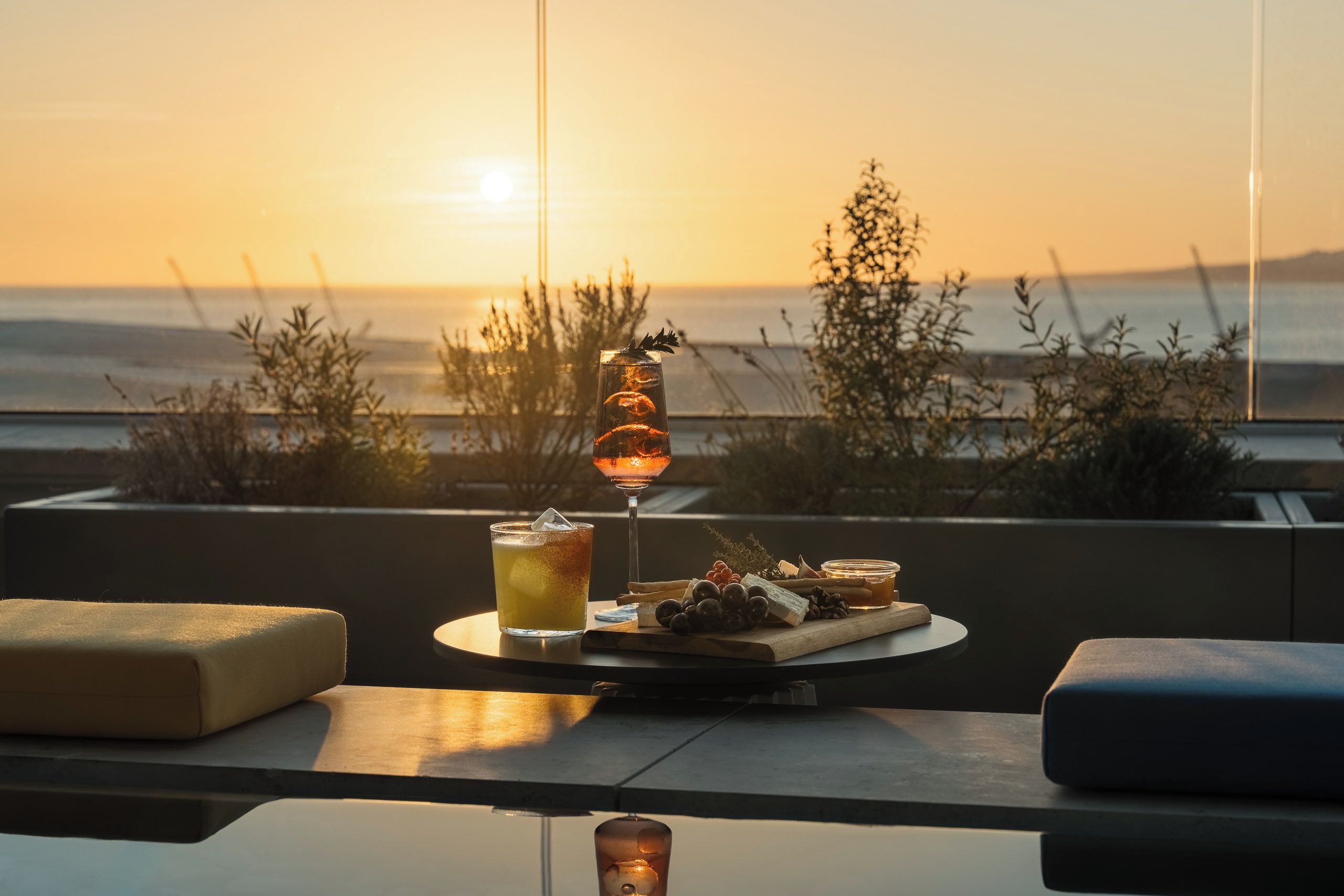 A table with a glass of iced beverage, a bottle of wine, and a cheese board with grapes and nuts.